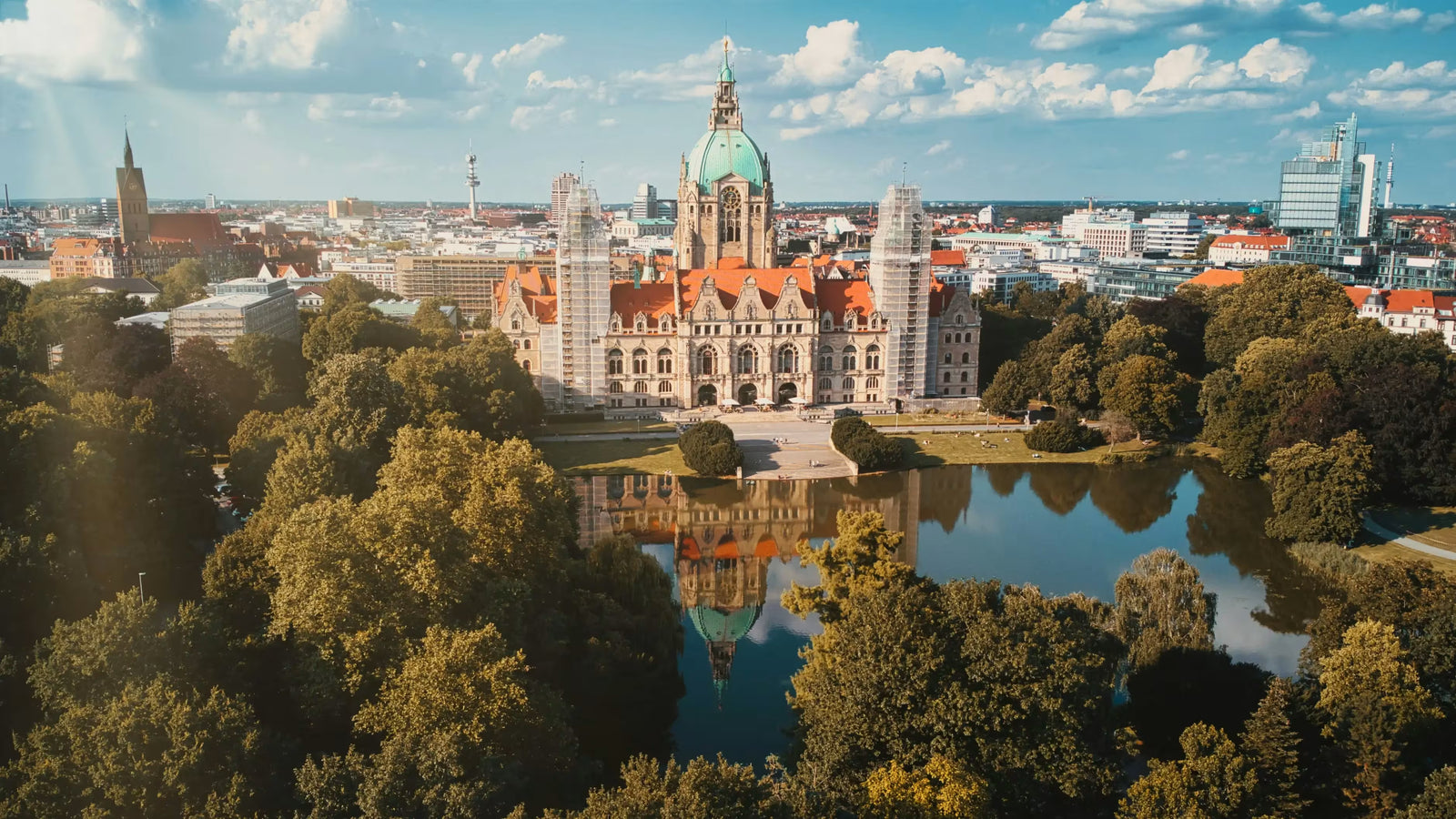 Luftaufnahme des Neuen Rathauses in Hannover mit Maschpark und Spiegelung im Wasser bei sonnigem Himmel
