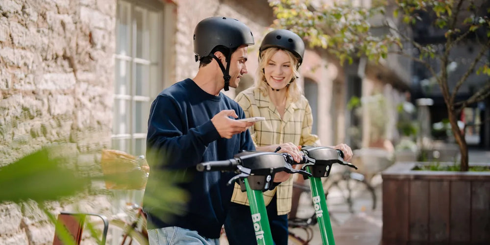 Junges Paar mit Helmen an Bolt E-Scootern in der Stadt