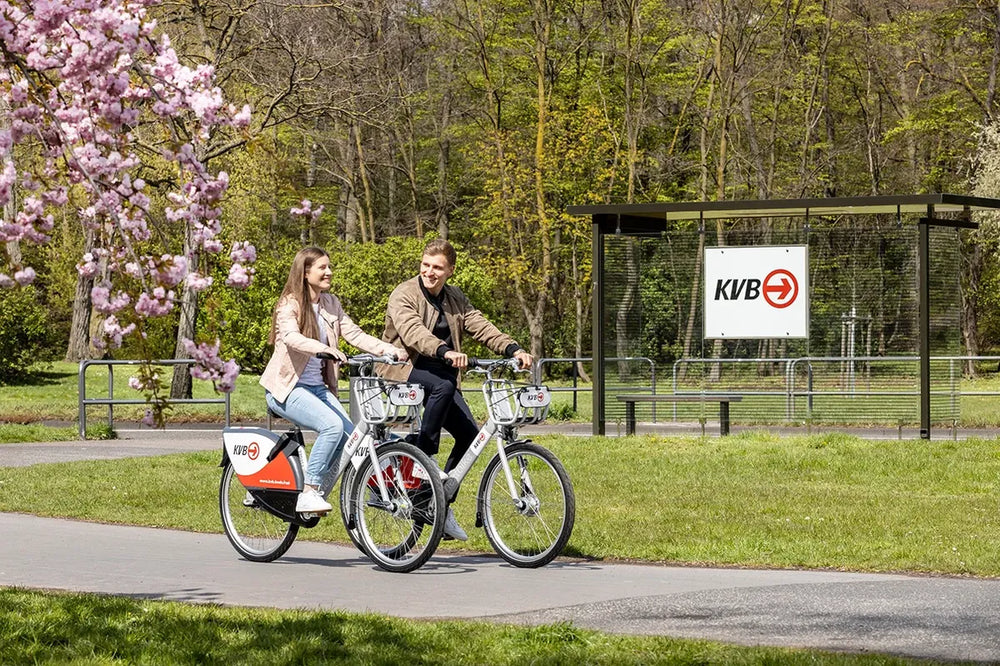 Paar auf KVB Leihrädern im Kölner Grüngürtel mit blühender Magnolie